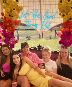 Girls sitting on event lounge with floral backdrop and neon sign